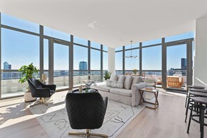 A spacious living room with large windows, a black chair, a sofa, and a dining area. - West Loop PH: Unmatched Views & Private Deck (Chicago)