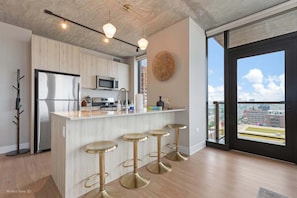 A modern kitchen with a central island, stainless steel appliances, and a view of the city through large windows.