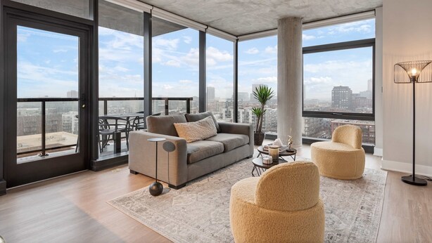 A modern living room with a grey sofa, beige armchairs, a coffee table, and a city view through large windows. - West Loop 2BR, Walk to Top Restaurants, Sleeps 5 (Chicago)