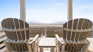 Area salotto esterna coperta con due poltrone Adirondack e un tavolino, con vista su una spiaggia e l'oceano.