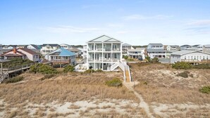 Una proprietà fronte spiaggia con diverse case, tra cui un edificio bianco ben visibile con un balcone, e una scala in legno che conduce alla spiaggia.
