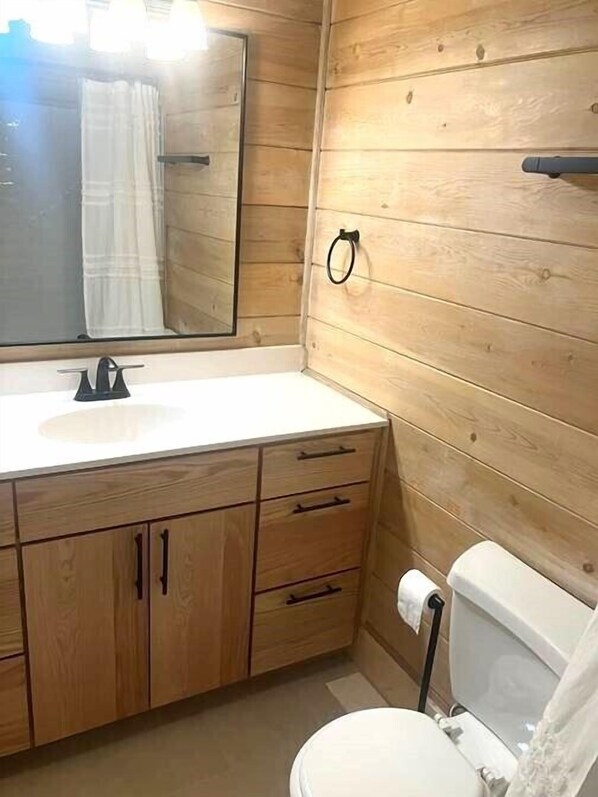 A bathroom with wooden panel walls, a white sink, a mirror, and a toilet. - Modern, Spacious Oceanfront Townhome Sleeps 10! (Ocean City)
