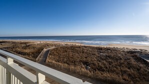 A beach view from a balcony with a wooden railing, sandy beach, and ocean. - Modern, Spacious Oceanfront Townhome Sleeps 10! (Ocean City)