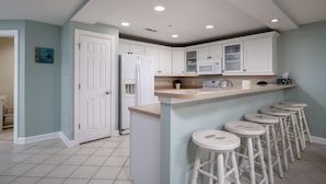 A kitchen with white cabinets, a refrigerator, a microwave, and a bar stool area.