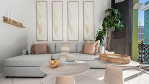 Un salon moderne avec un canapé gris, trois tableaux abstraits encadrés, une petite table ronde surmontée d’un panier en osier et une plante en pot.