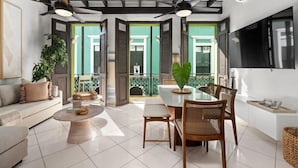 Un salon moderne comprenant un canapé, une table basse, une table à manger et des chaises. On y trouve également des ventilateurs de plafond, un téléviseur et un balcon avec vue.