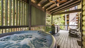 Un bain à remous sur une terrasse en bois, avec une clôture en bois, un ventilateur de plafond et un barbecue.