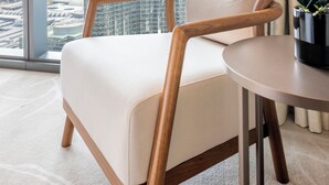 Habitació d'hotel moderna amb una finestra gran que ofereix vista a la ciutat, una cadira còmoda, una taula petita i una orquídia en test.