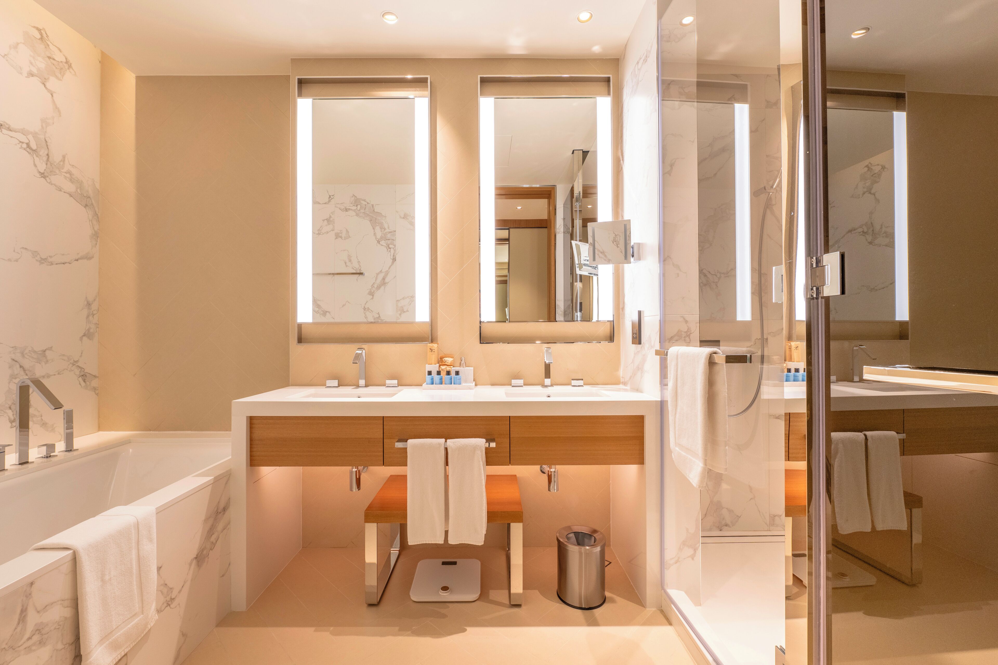 A modern bathroom with a marble wall, a large mirror, a bathtub, and a vanity with two sinks.