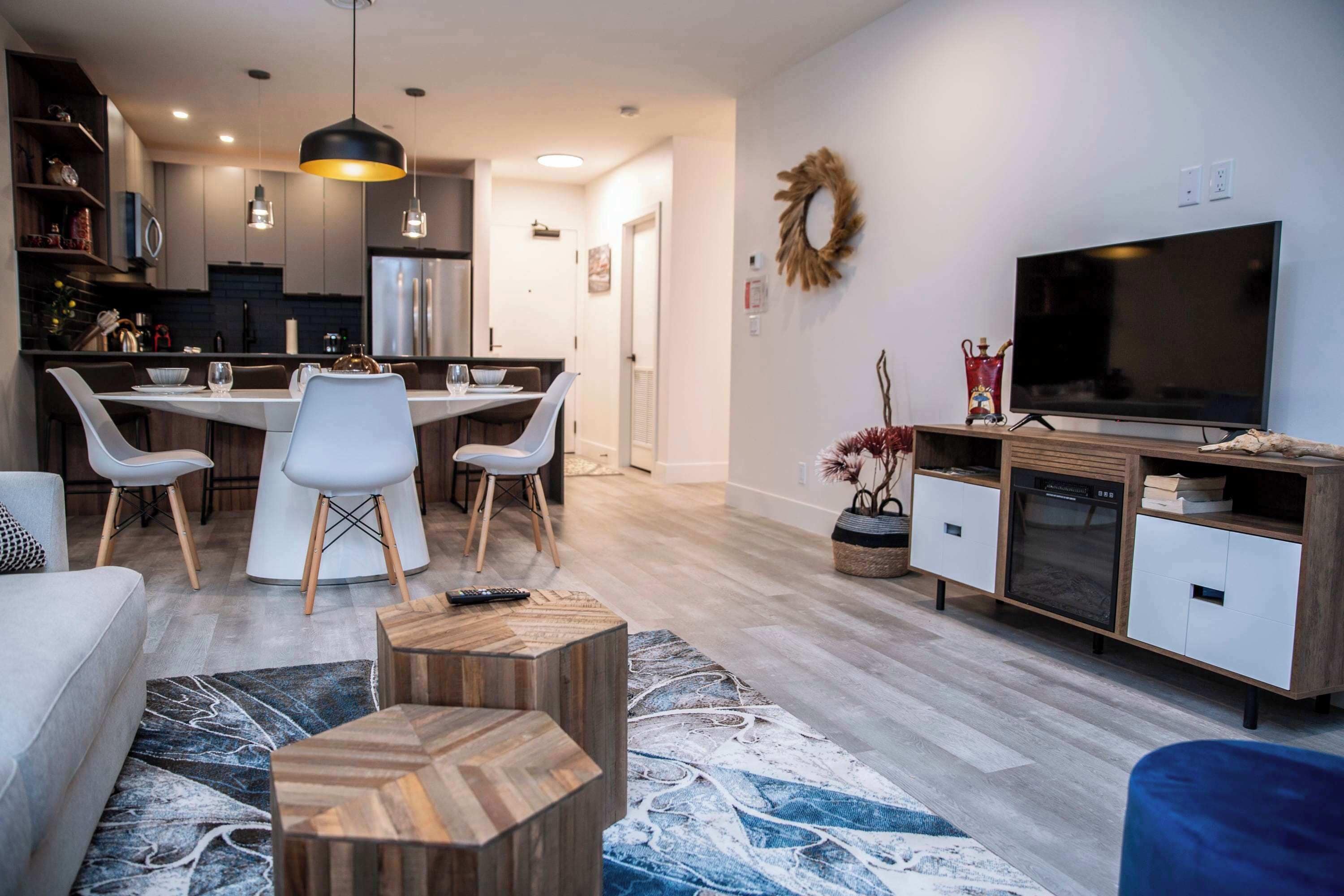 Una sala de estar moderna con comedor, televisor y cocina al fondo.