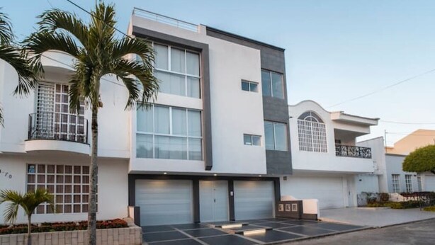 Un moderno edificio residencial de varios pisos con garaje, palmeras y césped bien cuidado.