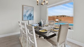 A dining area with a table set for four, white chairs, a chandelier, and a view of a swimming pool. - Zion Village Private Poolside Home (Hurricane)