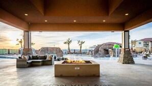 A covered outdoor lounge area with a fire feature, seating, and a view of the beach and ocean. - Zion Village Private Poolside Home (Hurricane)
