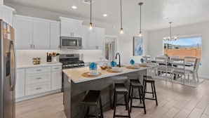 A modern kitchen with white cabinets, a central island with bar stools, a microwave, and pendant lighting. - Zion Village Private Poolside Home (Hurricane)
