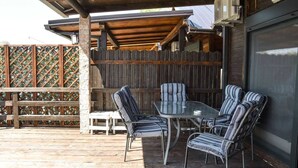 Um pátio externo com mesa e cadeiras, um deck de madeira e uma área coberta com cerca de madeira.