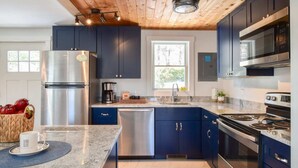 Une cuisine moderne avec des meubles bleu foncé, des appareils en acier inoxydable et un plafond en bois.