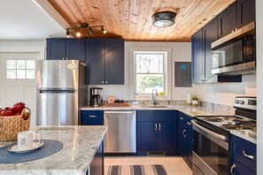 Eine moderne Küche mit Edelstahlgeräten, dunkelblauen Schränken und einer Holzbalkendecke.