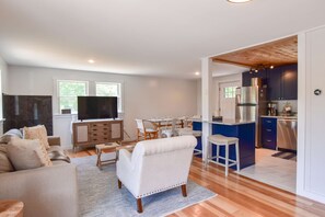Een moderne woonkamer met een flatscreen televisie, een bank en een eethoek met stoelen.