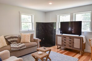 A living room with a sofa, a television on a wooden cabinet, and two windows. - 5 Min. Drive to Fisher Beach and Pamet Harbor! (Truro)