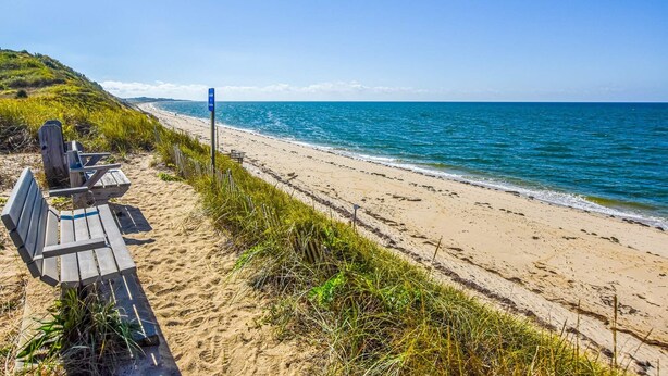 Une plage avec un banc en bois et un panneau indicateur.