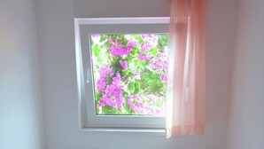 Une chambre avec une fenêtre, un lit avec une literie blanche et une tête de lit en bois.