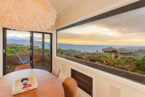 A dining area with a view of the ocean and houses, a woven ceiling light, and a table with a tray.