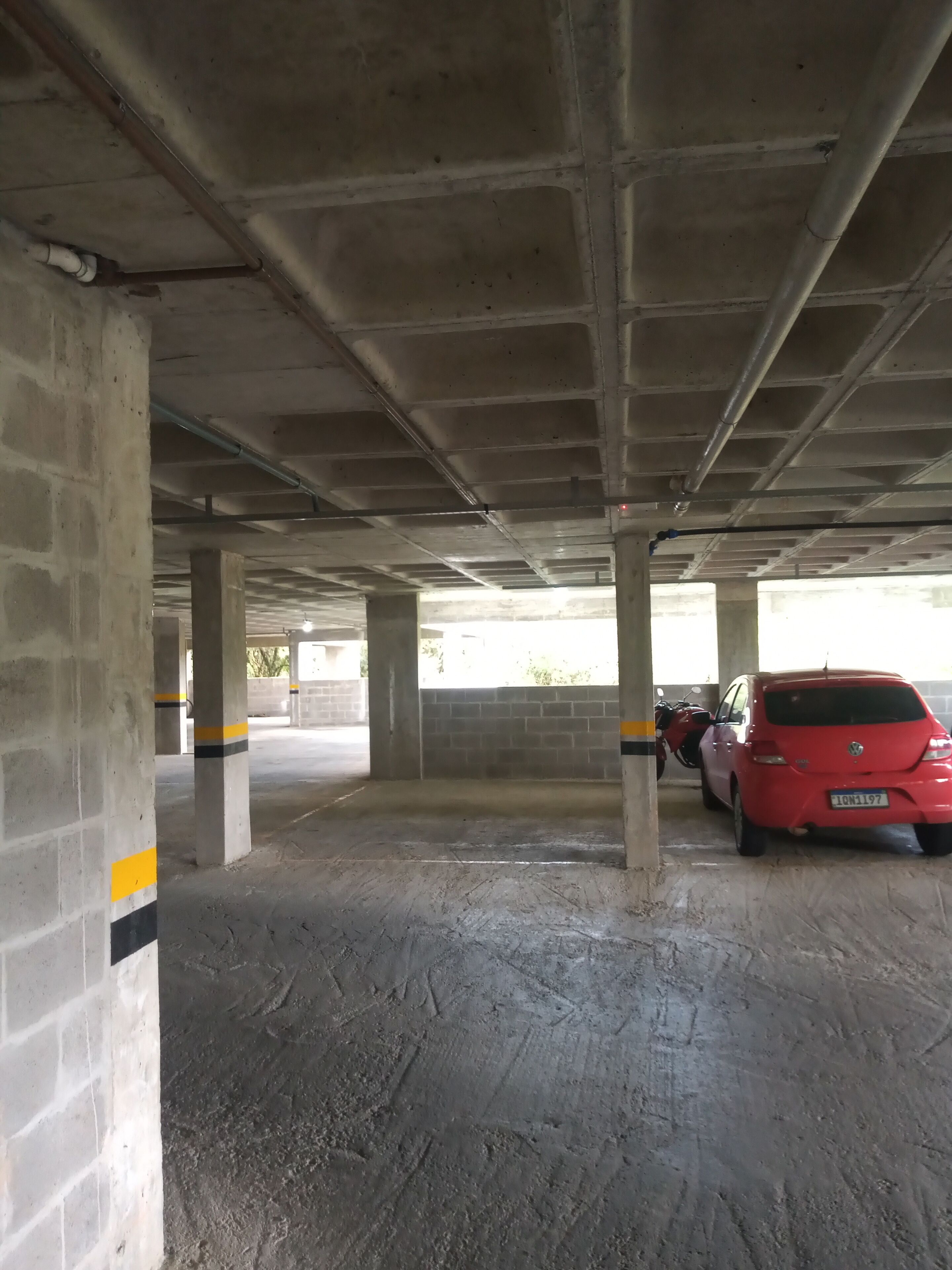 An underground parking garage with concrete pillars and a red car parked.