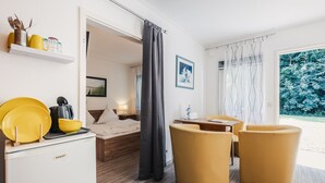 A modern hotel room with a bed, a desk, two yellow armchairs, a small kitchenette, and a view of the outdoors. - Küstenhostel (Klausdorf)
