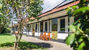 A row of white buildings with a red-tiled roof, numbered 2, featuring large windows and a small garden area with benches. - Küstenhostel (Klausdorf)