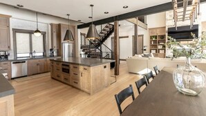 A modern kitchen with wooden cabinets, a central island, pendant lighting, and a staircase leading to an upper level. - Lodge at Cutthroat Landing- 20 mins to Yellowstone+Hot Tub+FirePit+Pickleball+LakeAccess+Henry'sLake (Island Park)