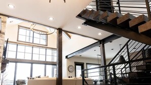 A spacious living area with a modern staircase, large windows, and a contemporary chandelier. - Lodge at Cutthroat Landing- 20 mins to Yellowstone+Hot Tub+FirePit+Pickleball+LakeAccess+Henry'sLake (Island Park)