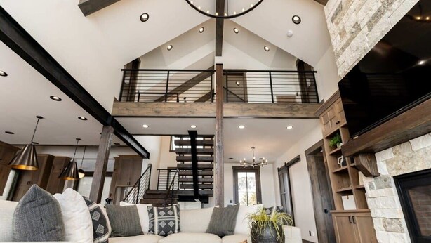 A spacious living area with a high ceiling, a staircase, a fireplace, and a large sofa with cushions. - Lodge at Cutthroat Landing- 20 mins to Yellowstone+Hot Tub+FirePit+Pickleball+LakeAccess+Henry'sLake (Island Park)