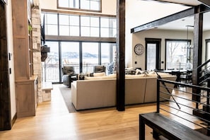 A spacious living area with a large window, a sofa, and a staircase. - Lodge at Cutthroat Landing- 20 mins to Yellowstone+Hot Tub+FirePit+Pickleball+LakeAccess+Henry'sLake (Island Park)