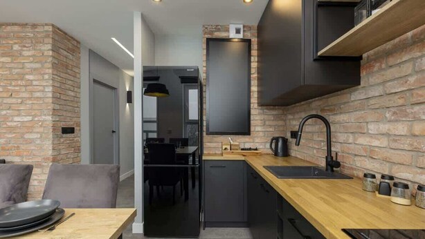 A modern kitchen with a brick wall, black cabinetry, and a wooden countertop. - Modern Apartment | 2 Bedrooms | Parking. (Lódz)