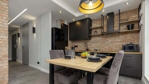 A modern kitchen with a brick wall backsplash, a wooden dining table, and grey upholstered chairs. - Modern Apartment | 2 Bedrooms | Parking. (Lódz)
