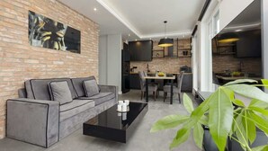 A modern living room with a grey sofa, a black coffee table, and a dining area with a table and chairs. - Modern Apartment | 2 Bedrooms | Parking. (Lódz)