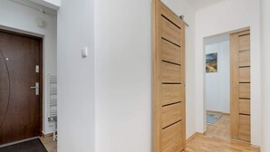 A hallway with wooden doors, a doormat, and a view of another room with a painting.