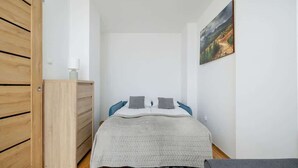 A bedroom with a bed, a wooden wardrobe, a nightstand, and a painting on the wall.