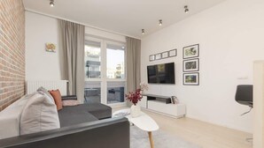 A modern living room with a sofa, a coffee table, a TV, and a balcony with a view of buildings. - Elegant Apartment with Balcony | Close to the Airport (Warszawa)