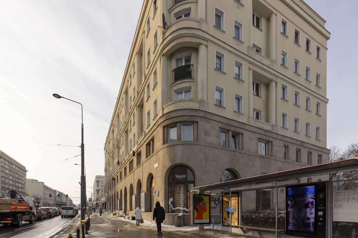 A multi-story building with a curved facade, a visible entrance, and a bus stop with a digital display.