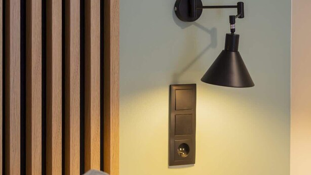 A modern bedroom with a wooden slat headboard, a bedside table with a small plant, and a wall-mounted lamp. - Modern Apartment | Workplace | Close to Metro (Warszawa)