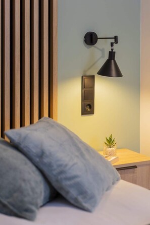A modern bedroom with a wooden slat headboard, a bedside table with a small plant, and a wall-mounted lamp. - Modern Apartment | Workplace | Close to Metro (Warszawa)