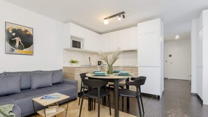 A modern living space with a grey sofa, a dining table with chairs, and a kitchen area with white cabinets. - Modern Apartment | Workplace | Close to Metro (Warszawa)