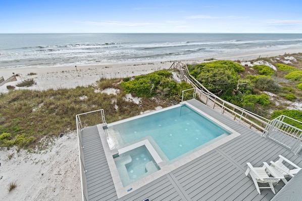 Relax by the ocean with a view of the beach from the pool deck, featuring a hot tub and lounge chairs.