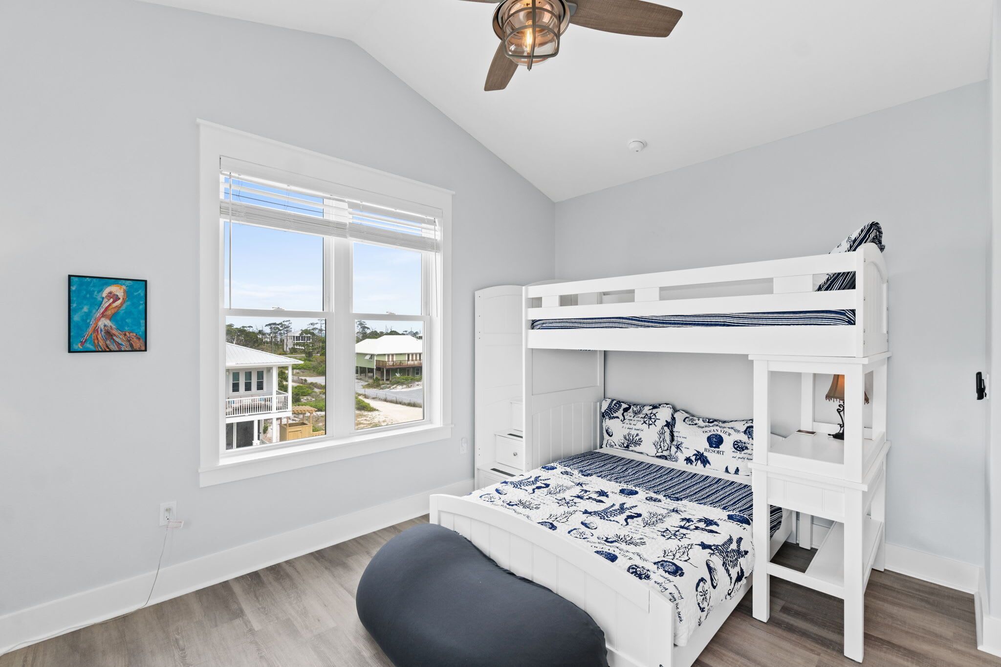 A bedroom with a bunk bed, a window with blinds, a ceiling fan, and a painting on the wall.