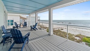 Une terrasse couverte avec des fauteuils Adirondack bleus, une table et une vue sur la plage et l’océan.