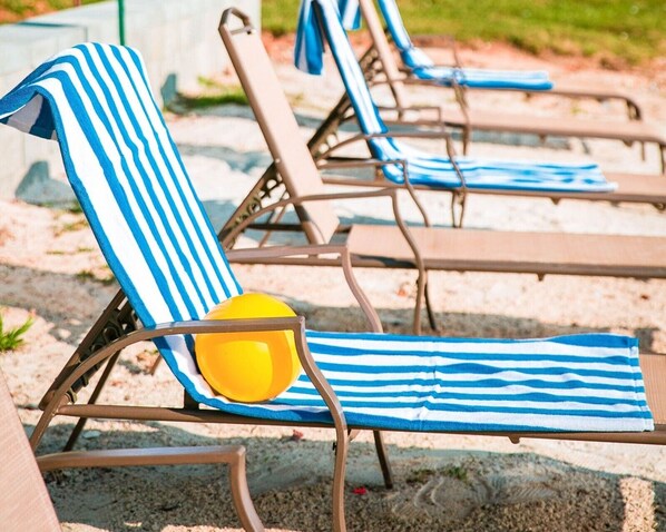 A row of sun loungers with blue and white striped towels and a yellow beach ball.