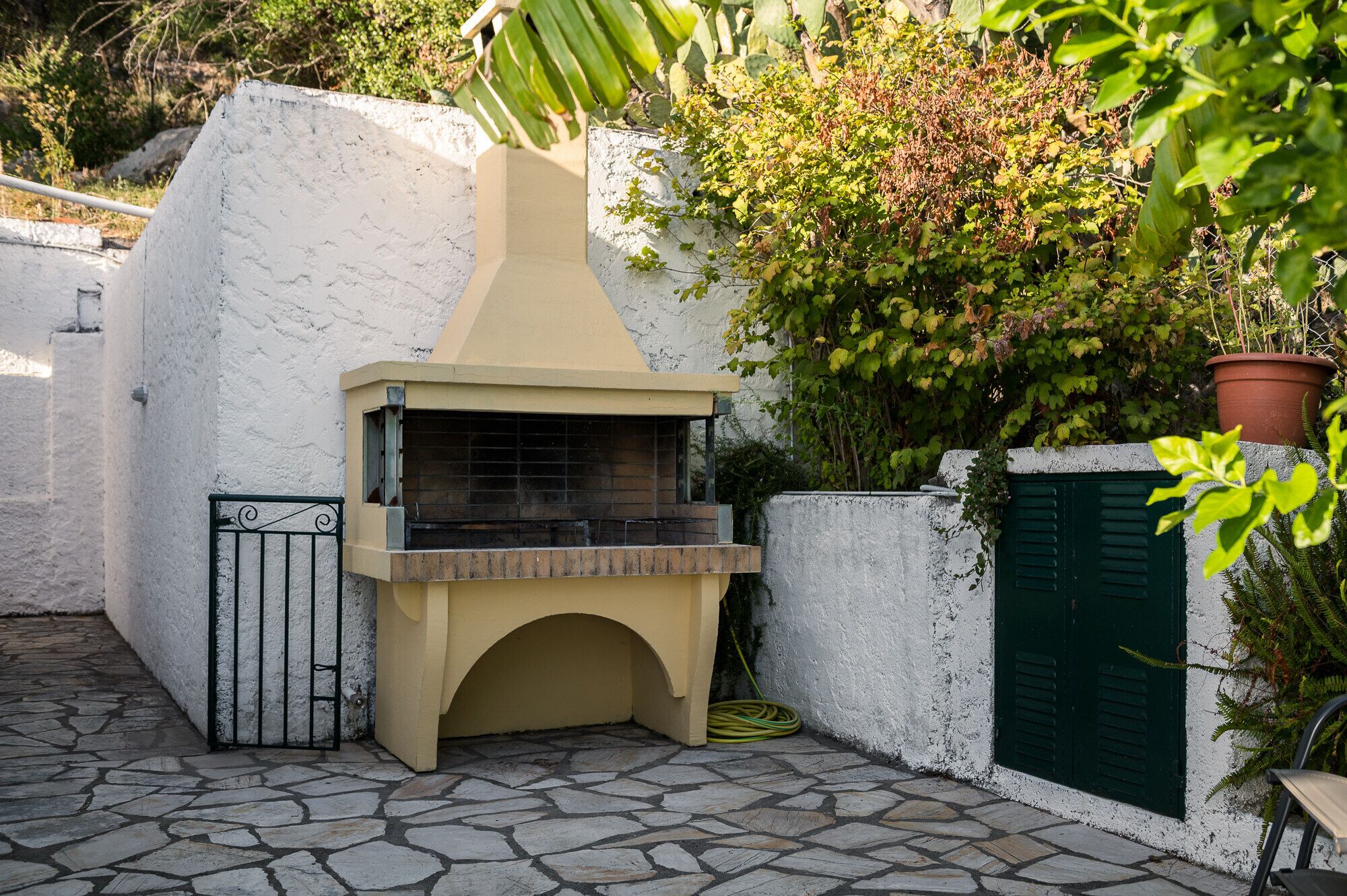 Une terrasse dallée de pierres, dotée d’un four extérieur encastré, d’un portail en métal et d’une plante en pot.