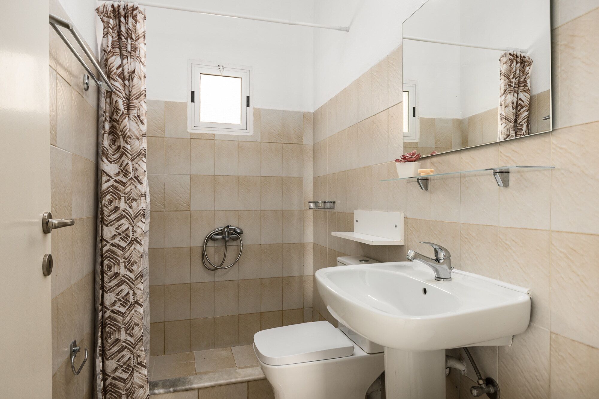 Ein Badezimmer mit Dusche, Toilette, Waschbecken und einem kleinen Fenster.