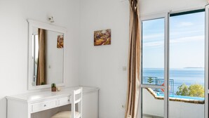 A bedroom with a white dresser, a chair, a large mirror, and a painting. There is a sliding glass door leading to a balcony with a view of the sea. - Four-Bedroom Villa Eleni by Konnect with Private Pool & Stunning Seaview (Corfu)